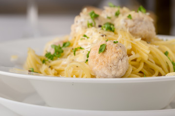Spaghetti with creamy chicken meatballs served on white plate with pine nuts. Close up