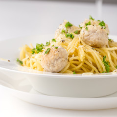 Spaghetti with creamy chicken meatballs served on white plate with pine nuts. Close up