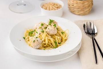 Spaghetti with creamy chicken meatballs served on white plate with pine nuts
