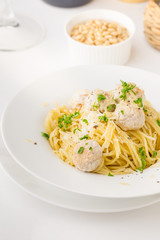 Spaghetti with creamy chicken meatballs served on white plate with pine nuts
