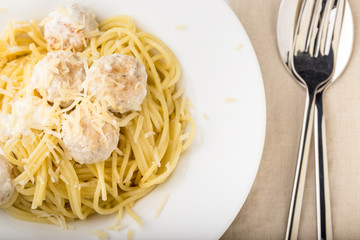 Spaghetti with creamy chicken meatballs served on white plate with pine nuts. Close up