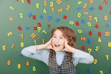 Girl stands in front of a green school board with magnets of numbers that depict her thoughts