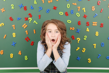 Girl stands in front of a green school board with magnets of numbers that depict her thoughts
