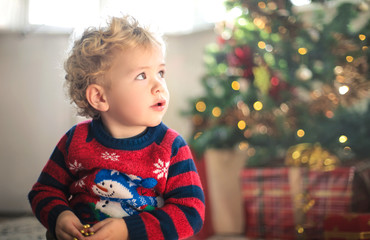 Fototapeta premium Beautiful child sitting on the carpet, surrounded by christmas gifts