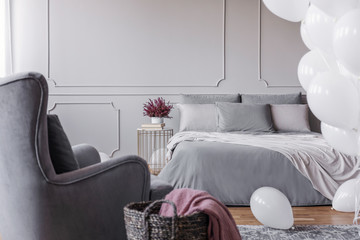 Trendy bedroom design with elegant double bed with grey sheets, comfortable armchair and heather on...