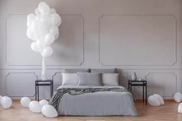 White balloons in spacious bedroom with king size bed with grey duvet and pillows between black...