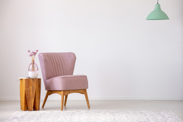 Flowers on wooden stool next to pink armchair in flat interior with copy space and mint lamp. Real...