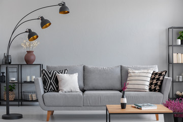 Industrial black metal lamp above stylish grey couch with patterned pillows, real photo with copy space