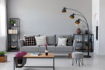 Copy space on the real photo of industrial living room with dark metal furniture and grey couch with patterned pillows