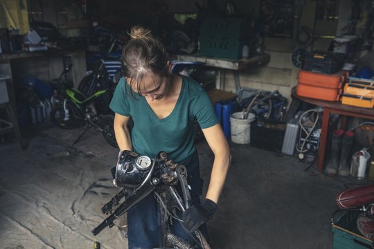 Female mechanic repairing motorbike in garage - Powered by Adobe