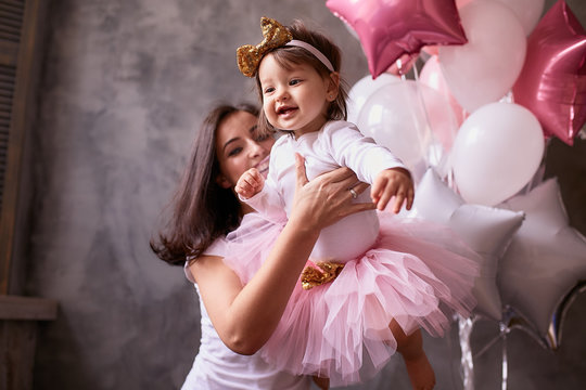 Lovely mom holds her little daughter tender standing in the room full of pink, white and silver balloons