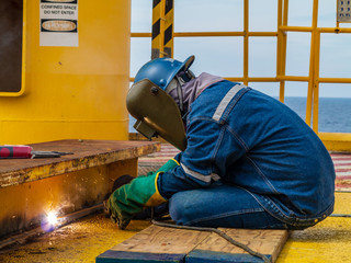 Industrial welder worker holding welding torch during perform welding sheet metal steel plate in construction factory by wearing heat protection gloves with smoke, spark, arc, fire, flash, hot