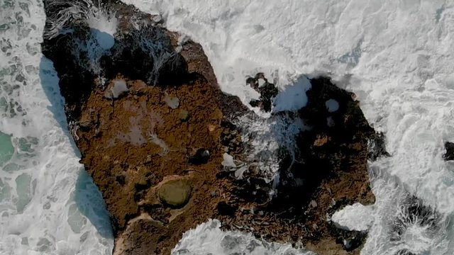 Rocks against ocean waves, overhead super slow motion view from drone