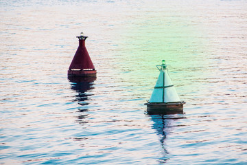 Two river buoys of red and white color with green light in calm river water.