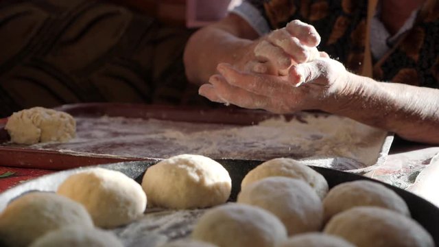 Grandmother's hands make cakes. Wrinkled female hands roll balls of dough. Knead the dough in the home kitchen.