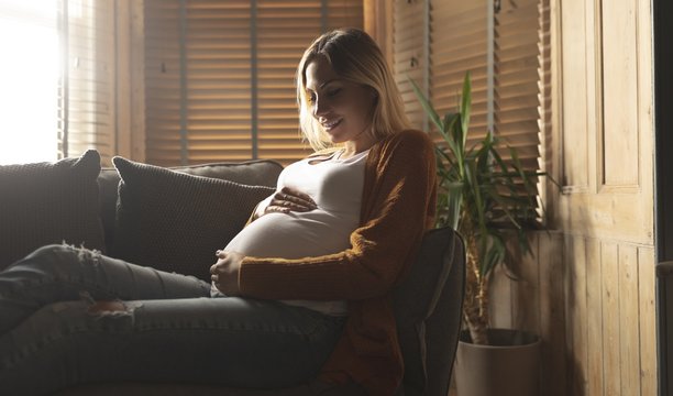 Pregnant woman sitting on sofa touching her belly