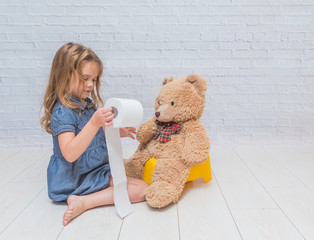 against the background of a white brick wall, the girl sits on a potty with the child, wiping her ass with toilet paper - obrazy, fototapety, plakaty
