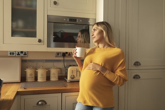 Thoughtful pregnant woman with bleached hair holding coffee cup