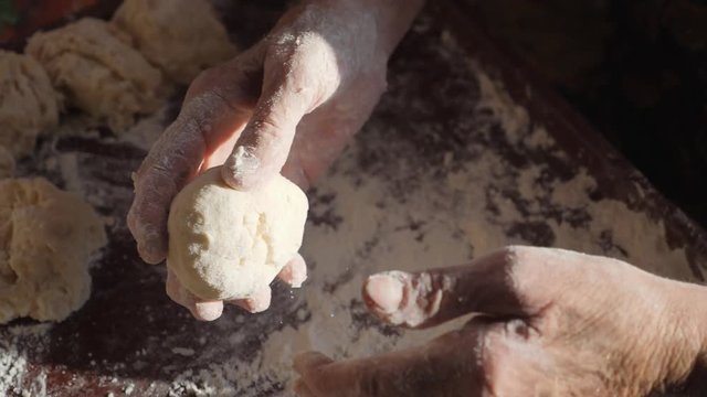 Grandmother's hands make cakes. Wrinkled female hands roll balls of dough. Knead the dough in the home kitchen.