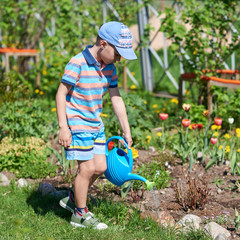 Cute European boy is watering flowers in the countryside croft. He is enjoying his job. © Artem