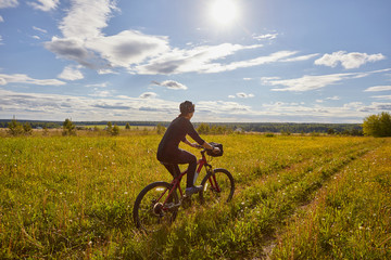 Obraz premium A young woman rides a bicycle on a field road. Summer sunny day