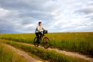 Fototapeta na wymiar A young woman rides a bicycle on a field road. Summer sunny day