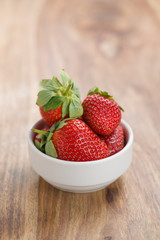 Fresh strawberries in white bowl on wood background with copy space
