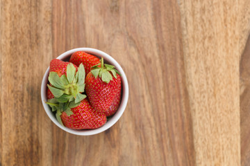Fresh strawberries in white bowl on wood background from above with copy space