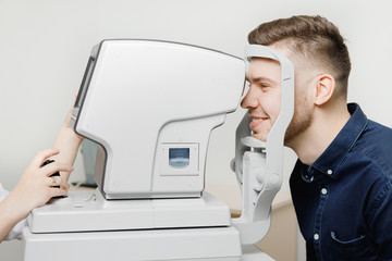 Beautiful smiling young stylish man with dark hair passes diagnostics of intraocular pressure...