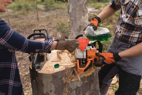 Two lumberjacks refuelling motor saw in forest - Powered by Adobe