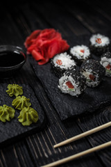 Minimalism and refinement: Tasty sushi with salmon and avocado are covered with black sesame seeds. Served with Ginger and Wasabi on the black stone.