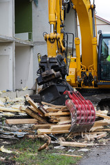 Fototapeta premium Demolition work. Excavator with grab breaking down a house.