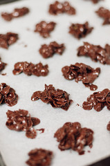 Chocolate covered cornflake cluster cookies, an easy and fun holiday or Christmas cooking project with kids, no-bake recipe for tiny cakes or semi-sweet cocoa snacks drying on parchment paper