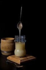 Glass jar with white honey and spoon at black background
