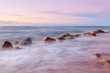 Sea sunset and big boulders sticking out from smooth wavy sea.