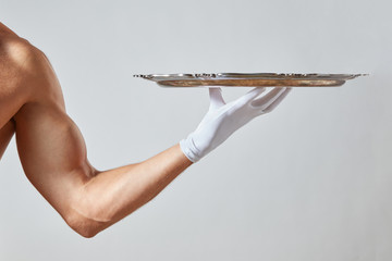 Muscular hand of waiter in a white glove holding a silver vintage empty tray on a white background.