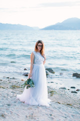 Fototapeta na wymiar young beautiful woman in elegant blue dress holding the bouquet of flowers and walking near the Garda lake, Sirmione. Lago di Garda, Italy