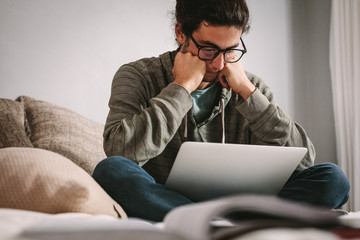 Tensed student looking at laptop sitting at home