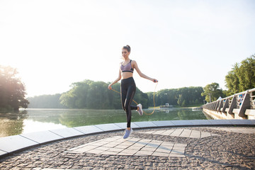 Portrait of fit young woman with jump rope in a park. Fitness female doing skipping workout...