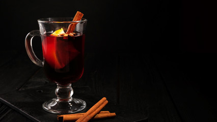 closeup glass of mulled wine with orange and cinnamon on dark black background, place for text