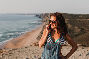 beautiful young woman on the top of a hill talking on her mobile phone and smiling. Summer time. Lifestyle