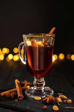 closeup glass of mulled wine with orange and cinnamon on dark black background,  christmas lights, large yellow bokeh, mulled wine set
