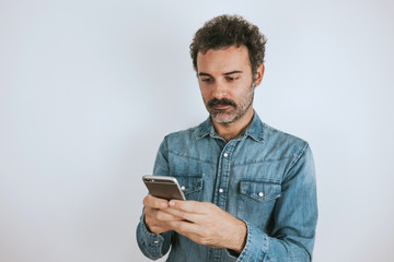 Portrait of brown, handsome man with mustache in jeans shirt using his smartphone. Gray background.