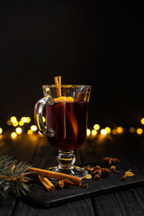 closeup glass of mulled wine with orange and cinnamon on dark black background,  Christmas tree and...