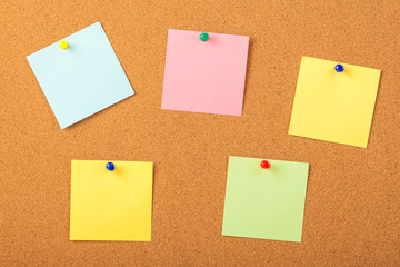 colorful papers pined with tacks on brown cork board background