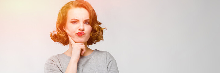 Charming young girl in a gray T-shirt on a gray background. The girl rested her hand on her chin