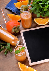 Orange smoothie in glass jars. Persimmon, orange pieces and a little blackboard with copy space