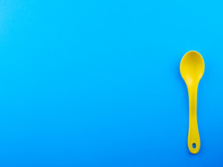 Yellow plastic spoon on blue background with copy space for text