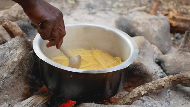 Close-Up Of African American Hand With Spoon Mix Pasta In A Pot On The Fire