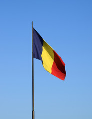 Romanian flag waving in the wind in front of a clean blue sky. Romania National Flag.